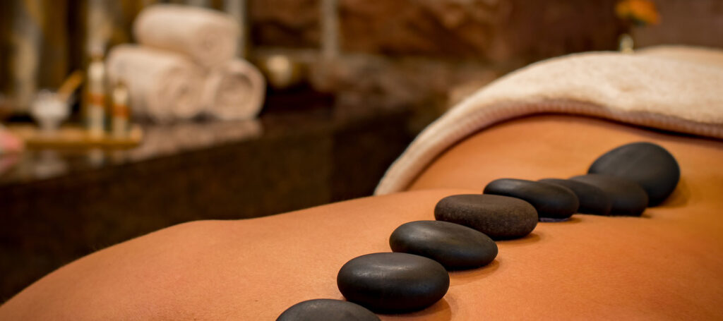 person getting a massage with black rocks lined up on their back